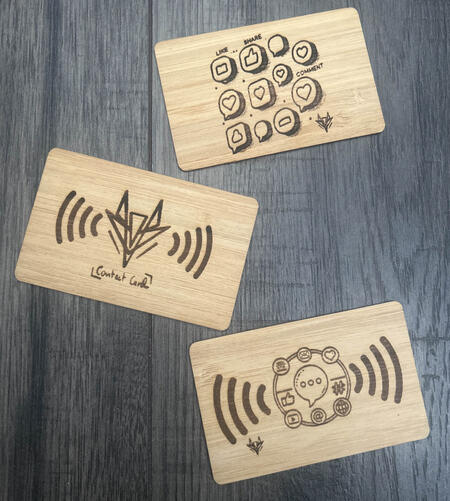 Three bamboo NFC business cards with engraved designs on a dark wood table
